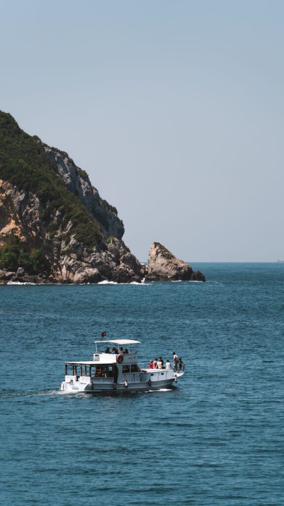 A boat with passengers sails near a scenic, rocky coastal island on a clear summer day.