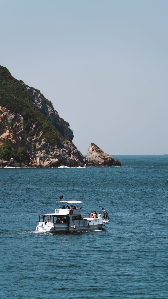 A boat with passengers sails near a scenic, rocky coastal island on a clear summer day.