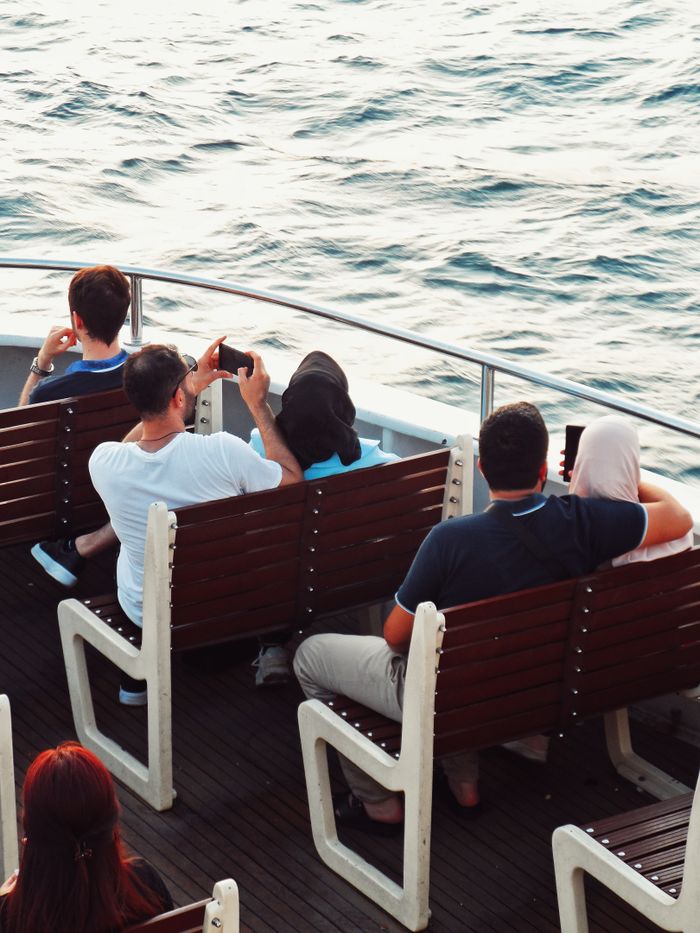 Group of adults relaxing on a boat, capturing the scenic view, a perfect summer day.