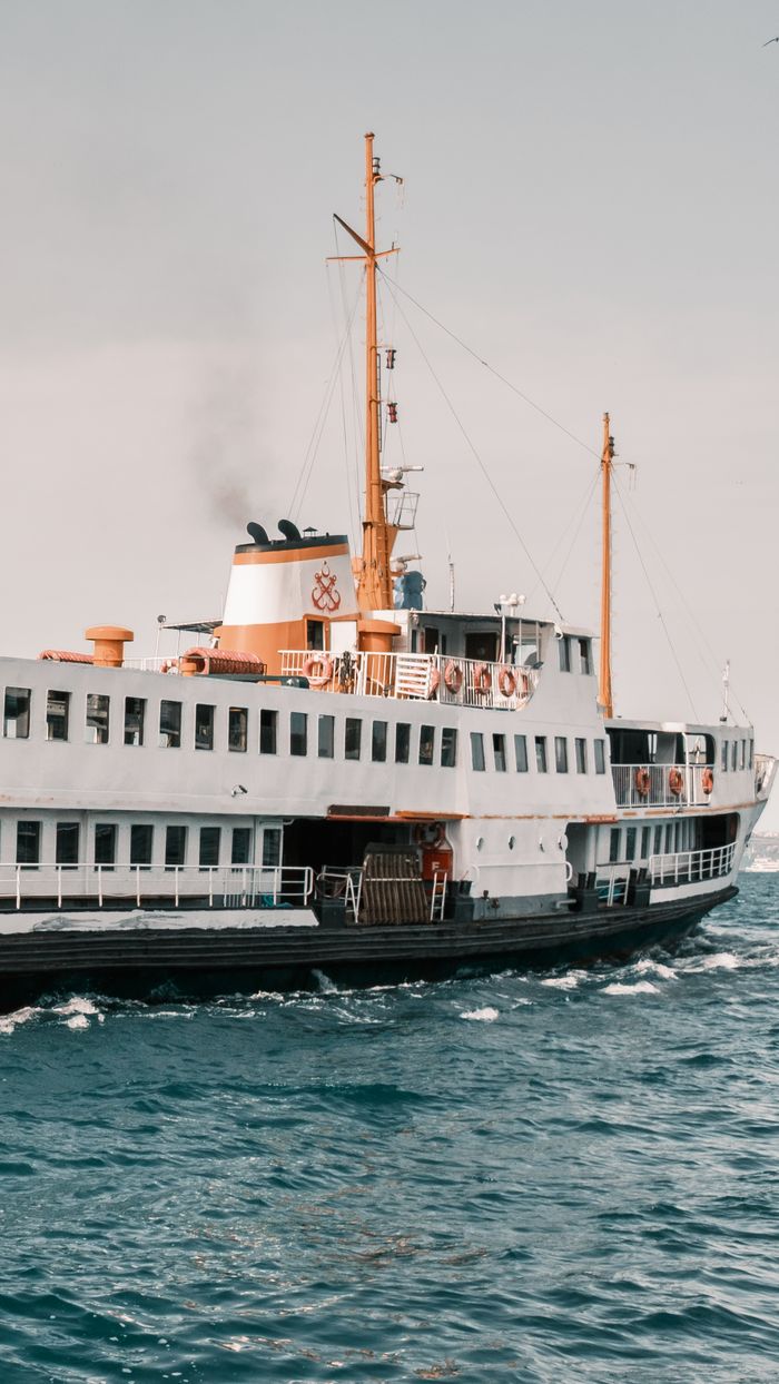 A vintage ferry cruises over blue ocean waves under a clear sky with visible smoke from the chimney.