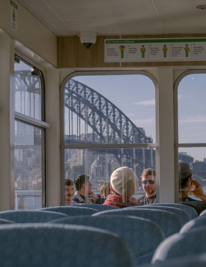 Travelers enjoying Sydney Harbour Bridge view through ferry windows on a sunny day.